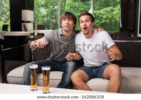 Two Male Football Fans Cheering Football Team. Drinking Bear In Pub, Green Trees On Background