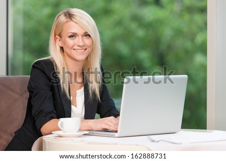 Smiling beautiful blond business woman with laptop. Drinking coffee at the restaurant