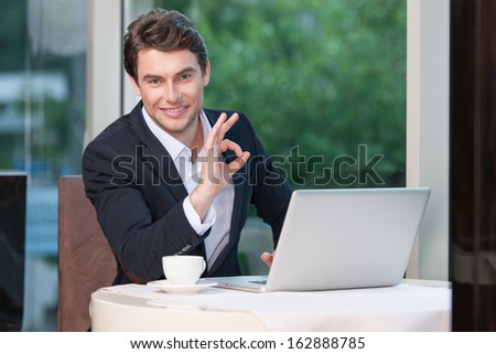 Attractive businessman showing ok sign. Smiling at camera sitting at restaurant