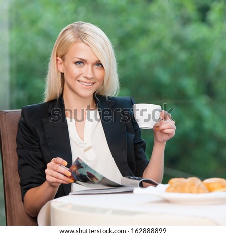 Attractive and stylish lady having breakfast. Reading magazine looking at camera