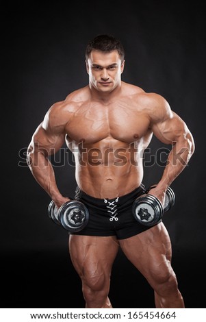 Sexy muscular bodybuilder lifting dumbbell. Training hands isolated over black background