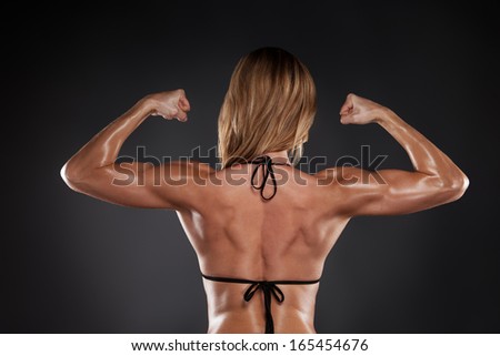 Muscular female back in black bikini. Back view isolated over black background
