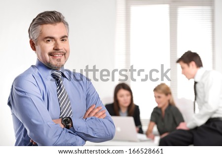 Close up of Grown up smiling successful business man. Standing on foreground and business team discussion on background