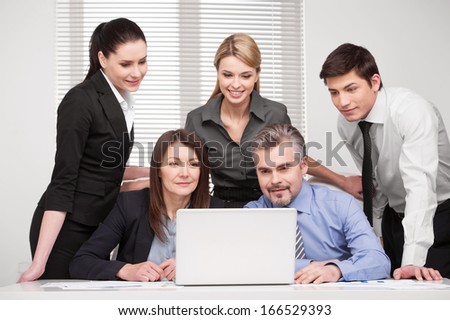 Large group of people looking together at laptop. Smiling and searching something, discussing ideas