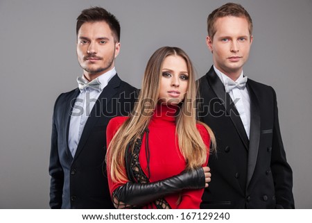 Sexy posing of one female blond model and two male models. Looking at camera and standing isolated over grey background