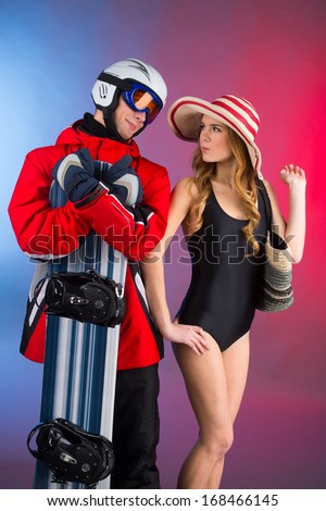 Beautiful woman in swimming suit standing together with handsome man in sport winter  costume with snowboard. Couple standing together over blue and red background