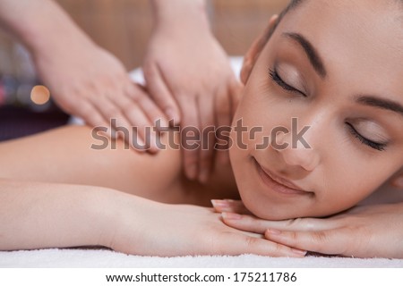 pretty girl on massage table. hand massage of back and candles on background