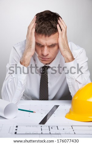 professional architect holding head and reading. man sitting at table and studying construction plan
