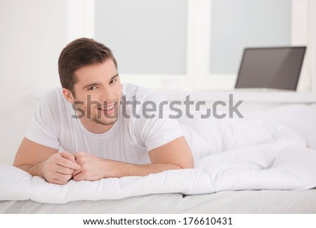 handsome white male laying in bed. man wearing white t-shirt smiling