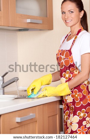 Beautiful young brunette washing dishes. attractive girl standing in apron and using detergents