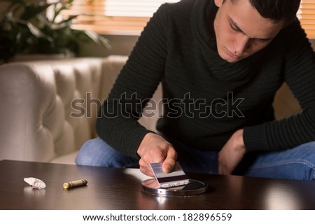 handsome man spreading cocaine on mirror. young guy holding credit card