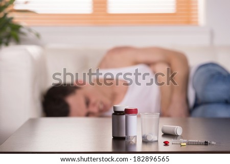young man lying on couch in pain. drug addict experiencing pain from pills