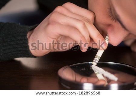 man snorting cocaine spread on mirror. guy holding dollar to inhale drug