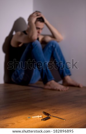 young handsome dude holding head. drug addict sitting in corner depressed
