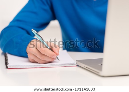 Student  writing. detail of a hand of man with blue shirt writing on a notebook with a pen
