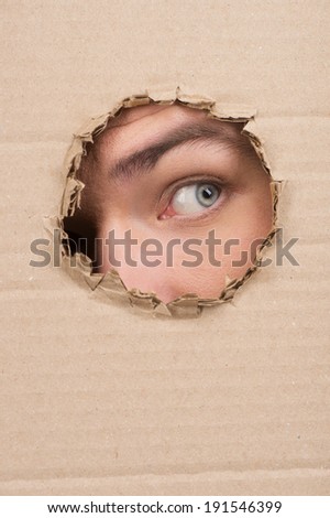 Through the looking hole. Closeup of an eye looking through a hole in a piece of cardboard