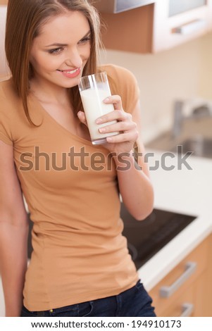 beautiful brunette drinking milk and smiling. waist up portrait of young woman standing in kitchen