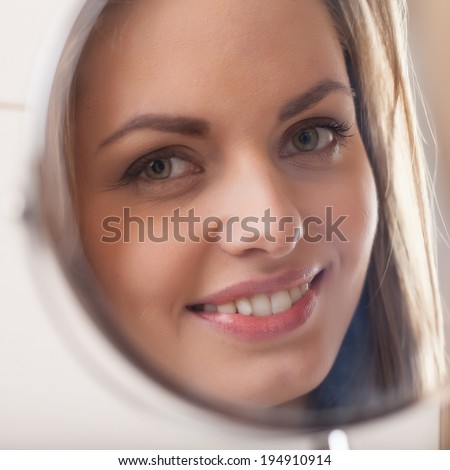 closeup of young woman looking into mirror. mirror reflection of beautiful girl smiling