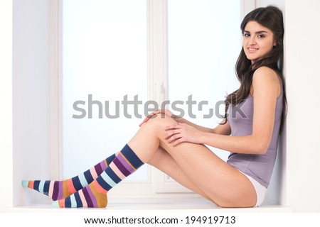 beautiful young brunette sitting on window sill. pretty lady wearing colorful knee socks