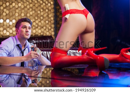 Handsome young business man watching striptease.  Sexy striptease dancer in red hose and high heel shows