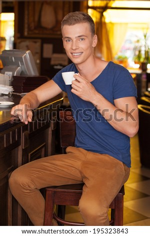 handsome guy sitting and drinking espresso. young man holding cup and smiling