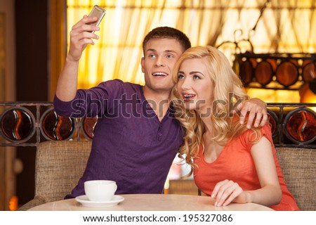beautiful couple making photo in cafe. man hugging woman and holding cell phone