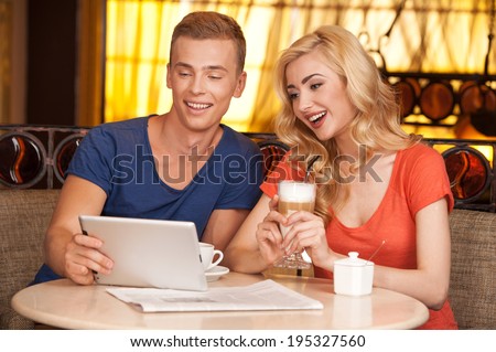 young couple sitting in cafe and resting. handsome guy showing on tablet and smiling
