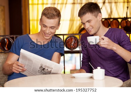two young man reading newspaper. handsome guys drinking coffee and talking