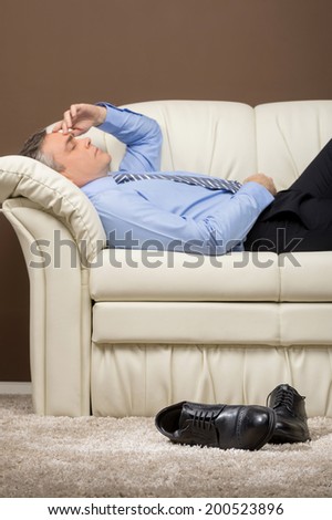 older businessman lying on white sofa. man took off shoes and sleeping on couch