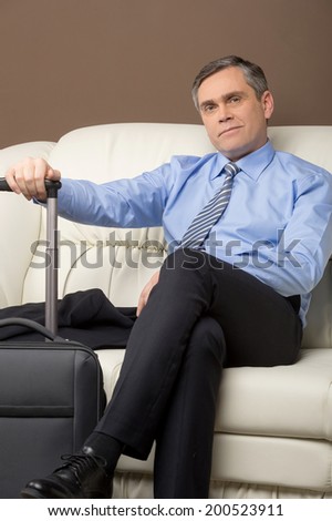 older man sitting on couch with luggage. man resting on sofa prepared to leave
