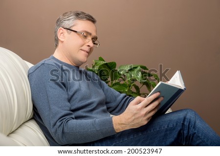 older man reading book on sofa. man sitting on couch and holding book