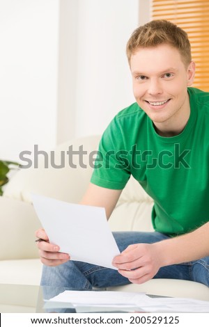 young man writting and holding paper. handsome guy sitting on couch and smiling