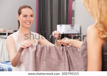 seller suggesting tissue to customer and smiling. back view of blond buyer holding fabric