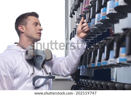 waist up of man selecting car paint. closeup of man wearing overall and working in shop