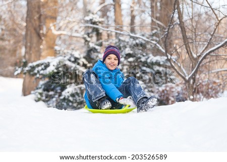 boy sitting on sledges and sliding down. child playing in park on snow in winter