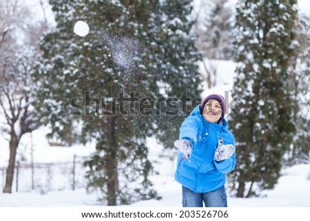 schoolboy playing outside and throwing snowballs. child wearing blue jacket in park