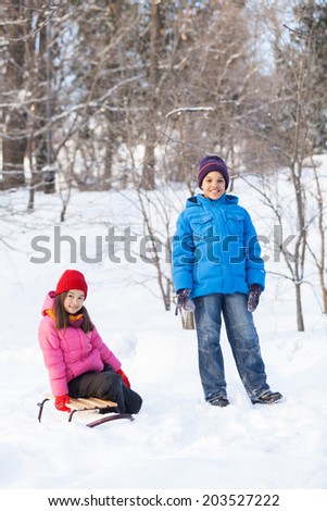 boy and girl playing outside on snow. girl sitting on sledges in park and smiling