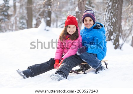 two children prepared to slide from hill. brother and sister sitting on sledges in park