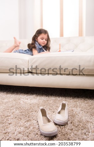 charming little girl writing in notebook. nice girl lying on white sofa