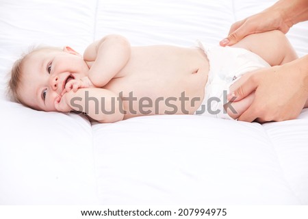 cute infant lying on white bed. mother holding legs of small baby
