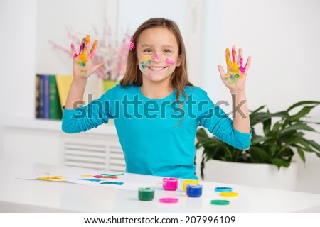 cute girl lifting hands stained with paint. waist up schoolgirl smiling and sitting at table