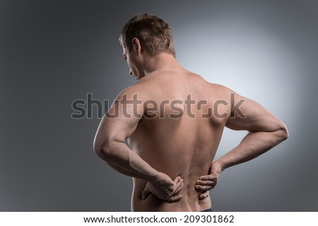 Close-up of young shirtless man with back pain. young man standing on grey white background