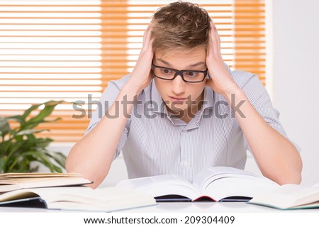 shocked male student working in studio. University student with many books at desk learning for exams