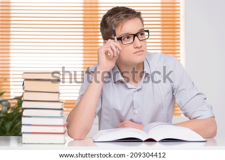 Focused male student working in studio. University student with many books at desk learning for exams