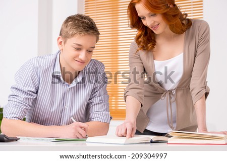young student preparing to exams and smiling. woman tutor standing and helping boy learning lesson