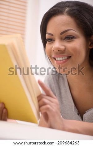 Good looking african american lady looking into book. young girl wearing grey sweater and reading book