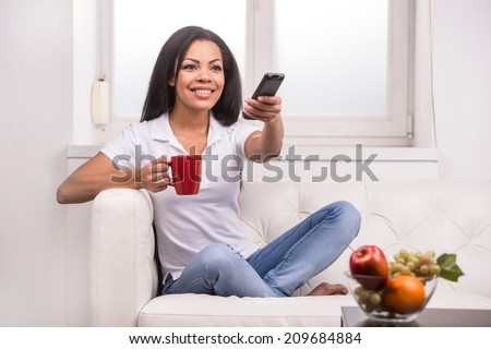 Woman watching tv at home and holding a remote control. Smiling woman on couch changing TV programme