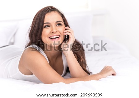 Beutiful happy woman talking at mobile phone. Undressed young girl lying on belly and talking