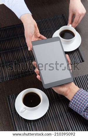 friends drinking coffee in cafe and showing news. two hands holding tablet over table.