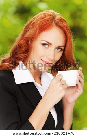 Redhead business girl with cup of tea. Woman with tea cup on background of green leaves